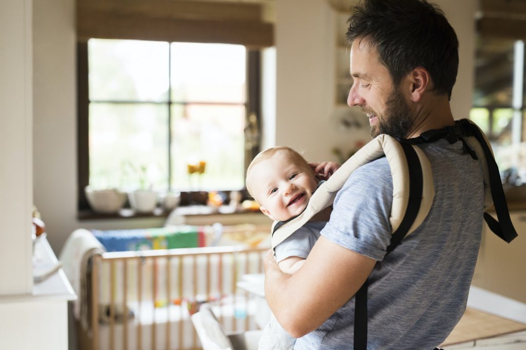 Happy father with baby in baby carrier at home