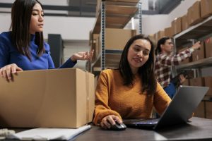 Warehouse women workers planning packages delivery schedule on laptop