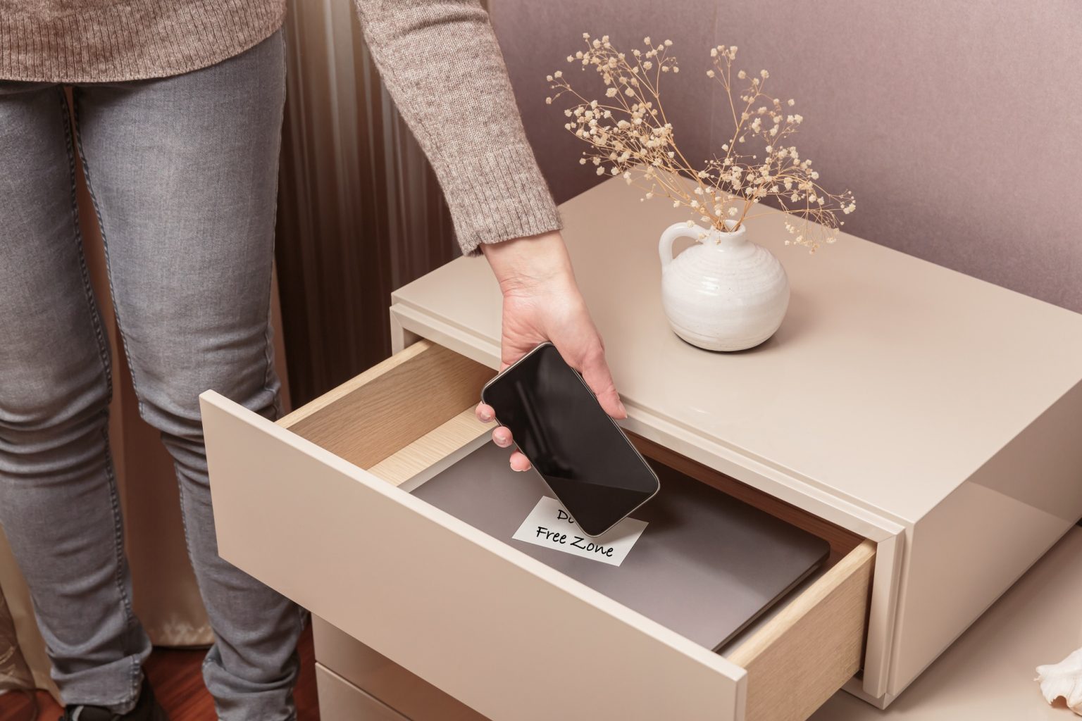 Woman putting her phone in drawer with different gadgets at home