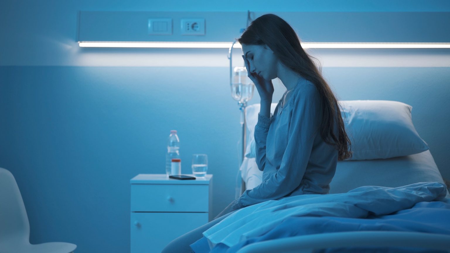 Sad sleepless patient sitting on the hospital bed at night